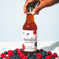 Bottle of 'mindful' sparkling kombucha surrounded by berries on a light background
